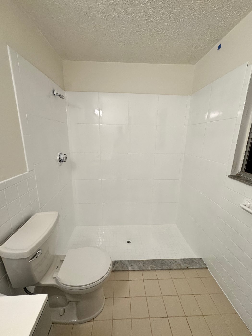 A shower area refinished from beige tile to bright white walls and floor