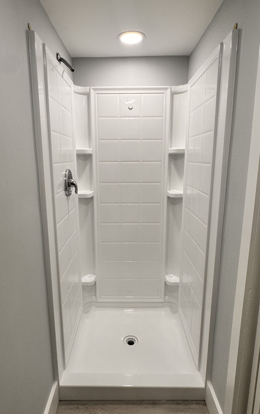 A clean white refinished shower stall with tile-pattern walls and built-in seat