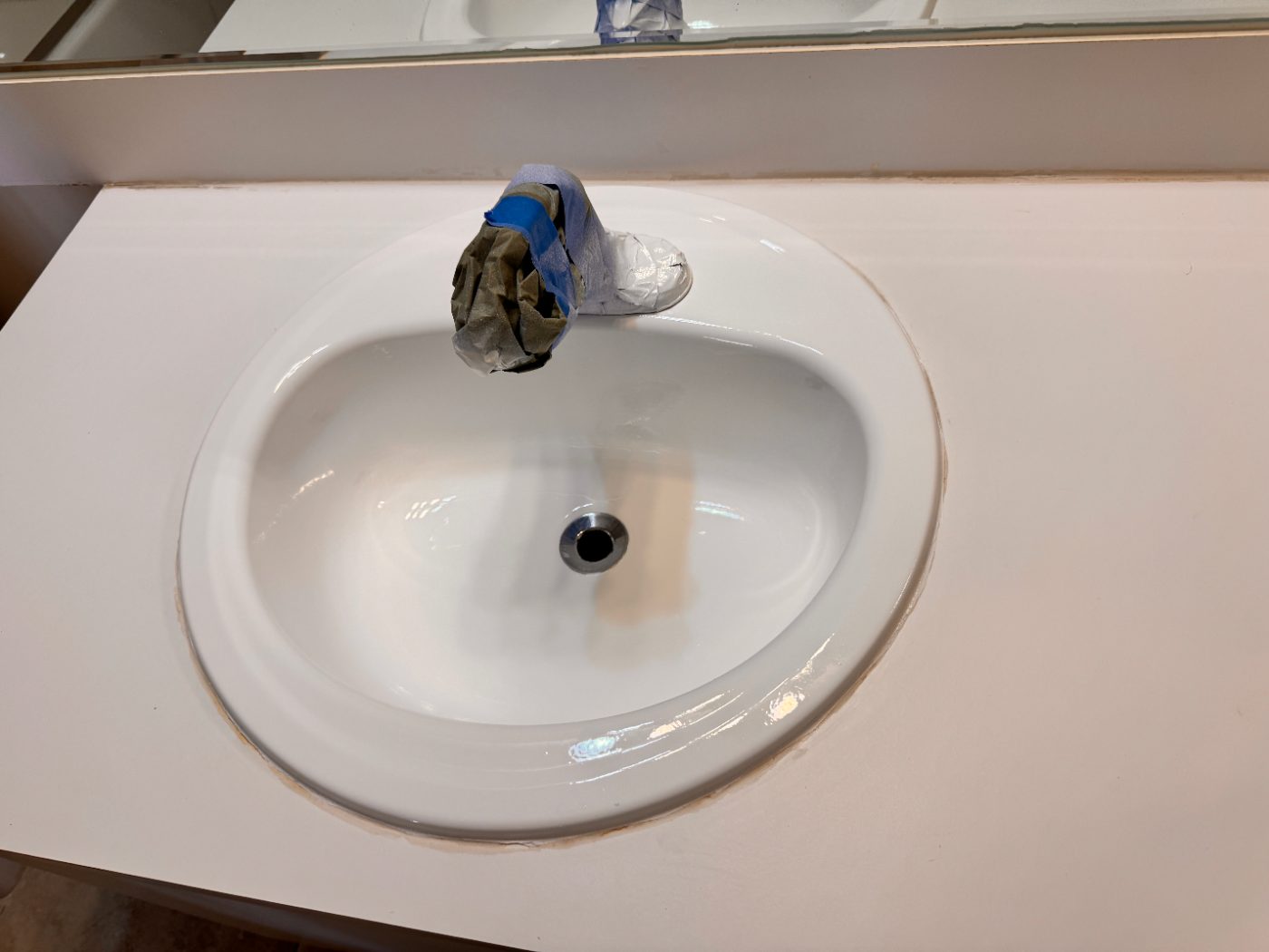A drop-in bathroom sink refinished bright white, faucet still wrapped