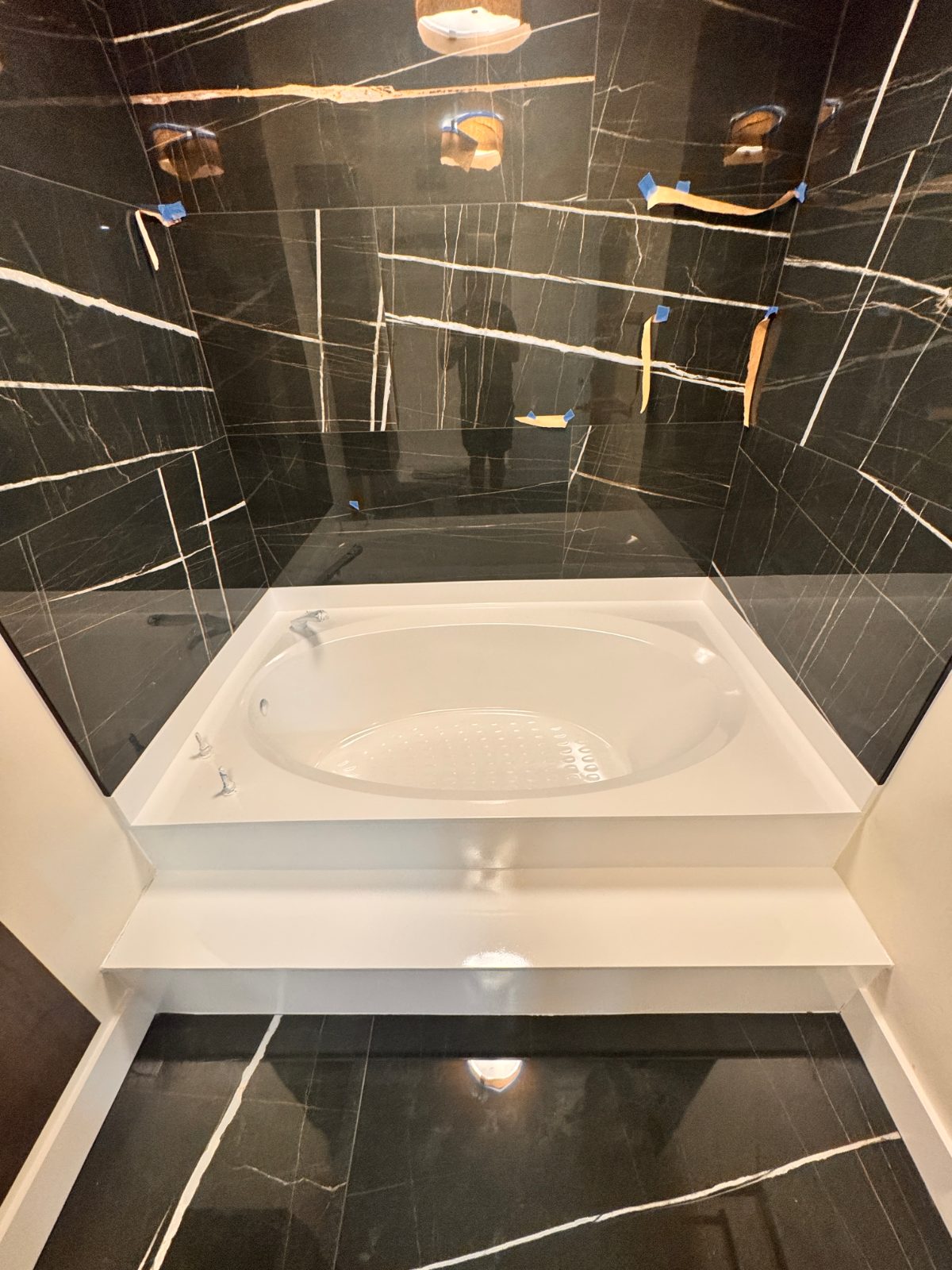 A drop-in spa tub refinished bright white in a black-marble bathroom remodel