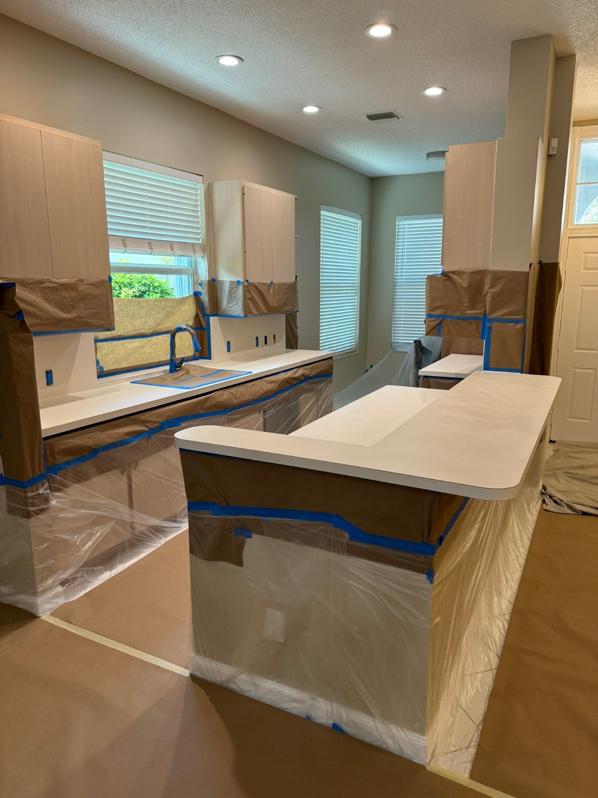 Kitchen fully masked for countertop refinishing — cabinets papered, floors covered, island wrapped