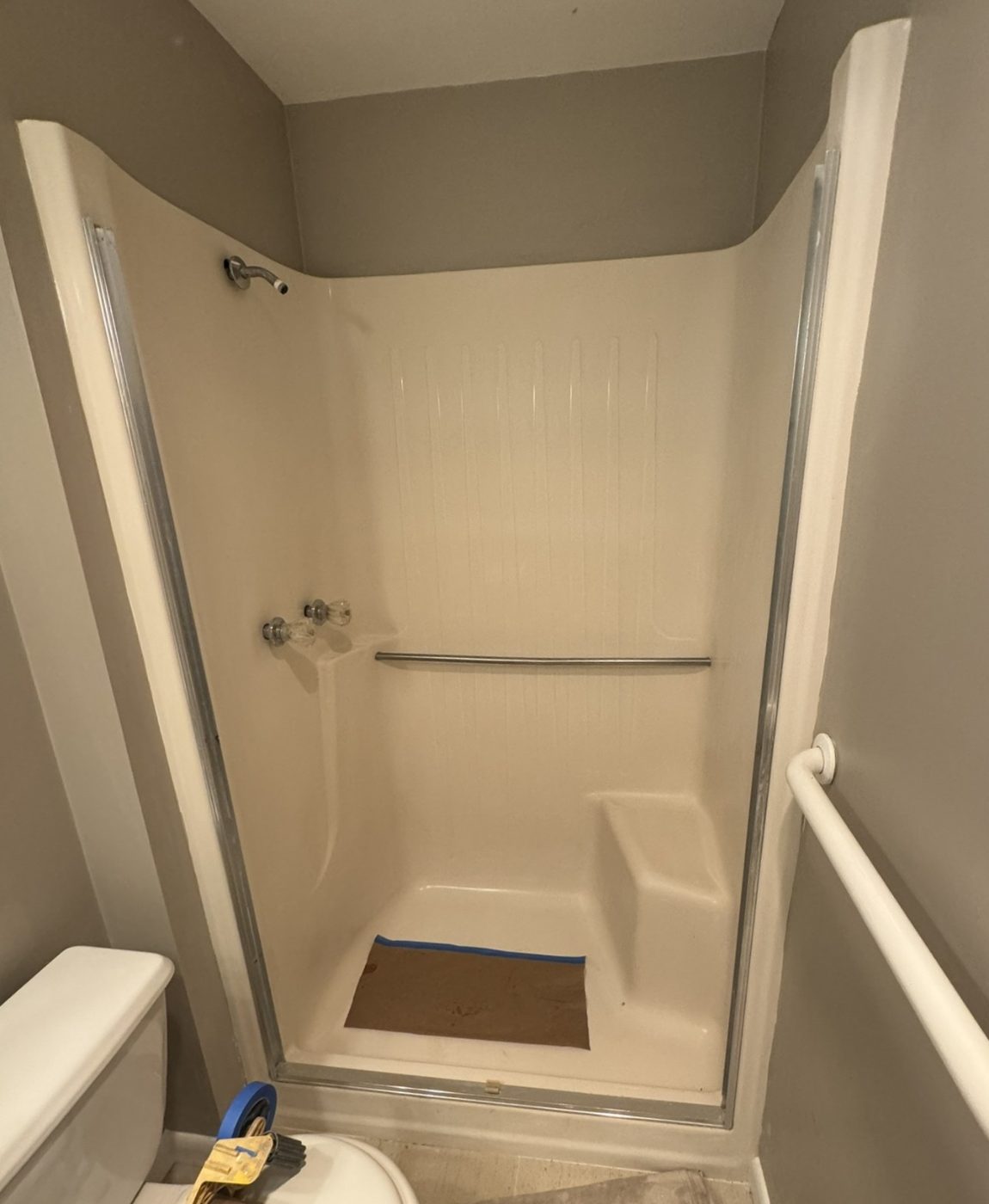 A worn fiberglass shower stall with grab bars, photographed before refinishing