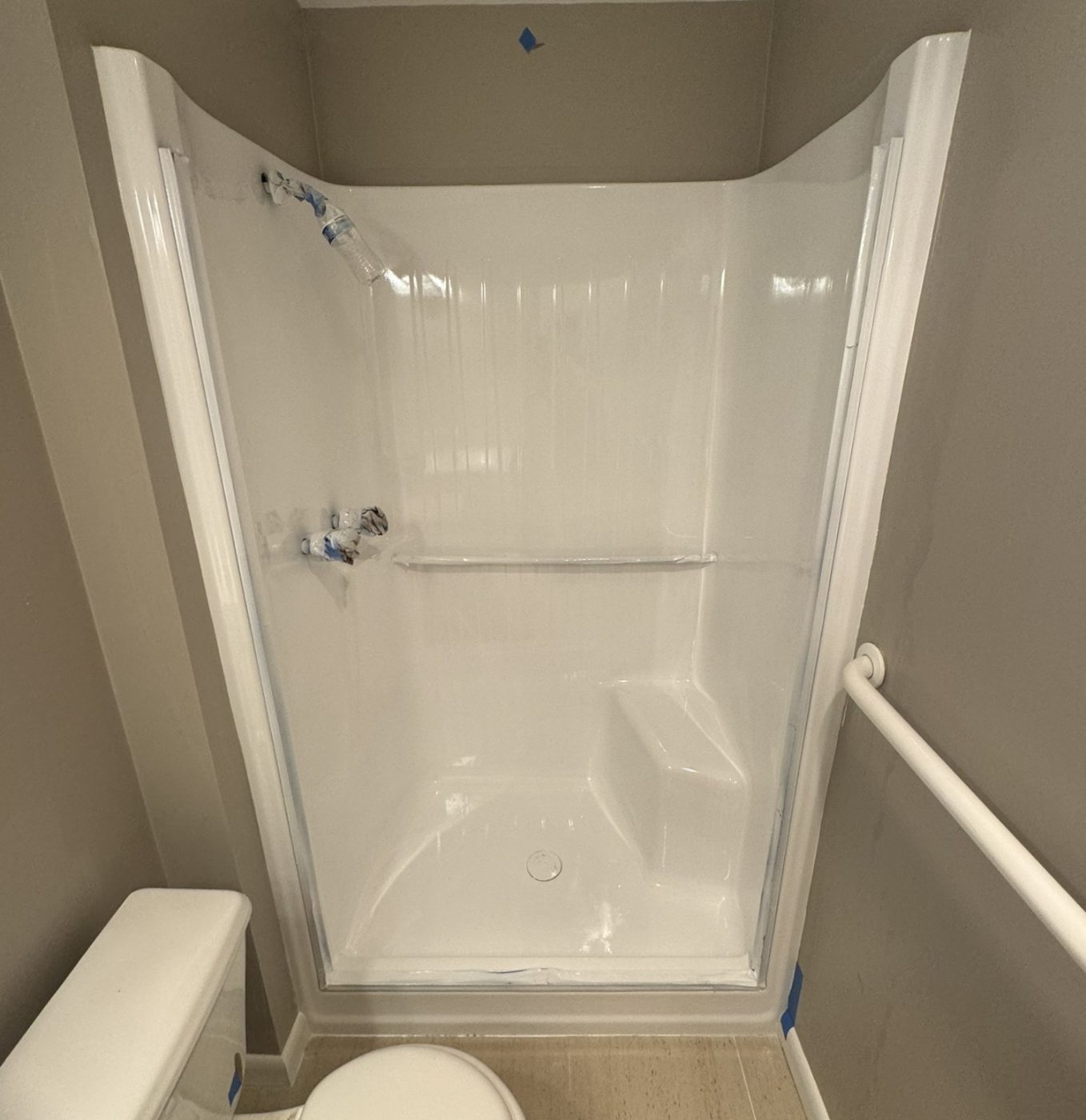 The same shower stall freshly sprayed bright white, fixtures still wrapped