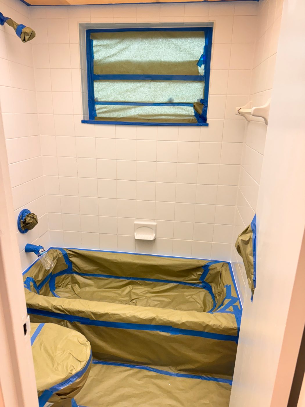 A tub alcove fully masked — window papered, tub tented, fixtures wrapped