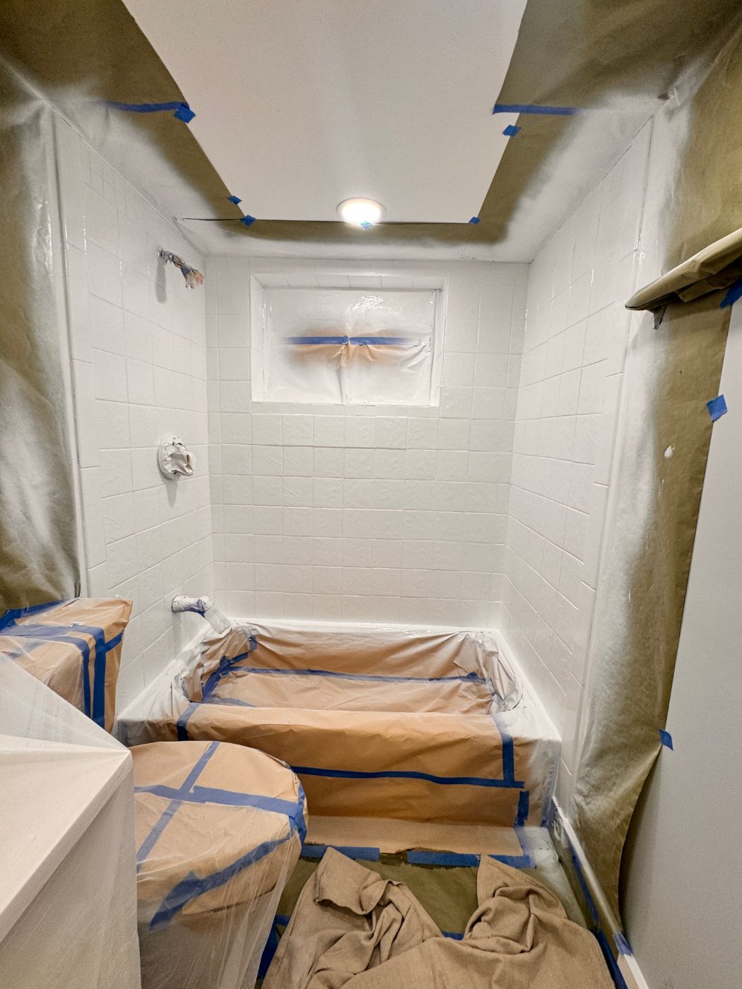 The tile walls freshly sprayed white while the tub is still masked