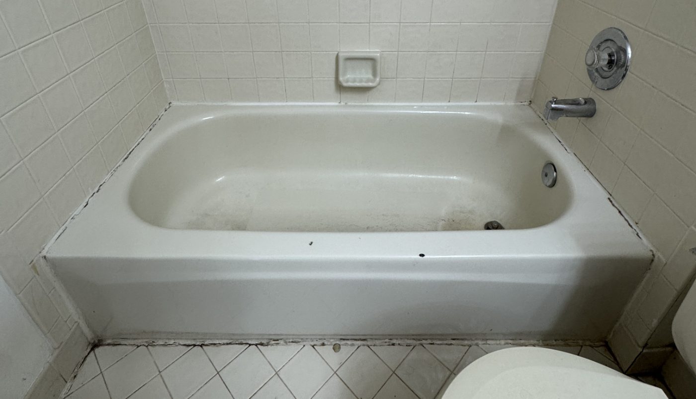 A worn bathtub with failing caulk lines, photographed straight on before refinishing