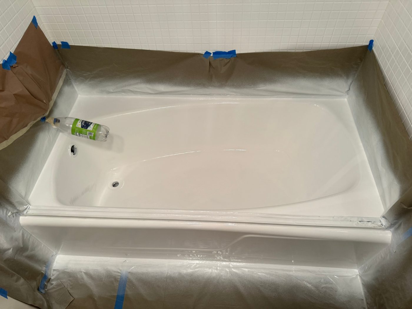 The same bathtub freshly sprayed to a uniform white gloss, masking still up