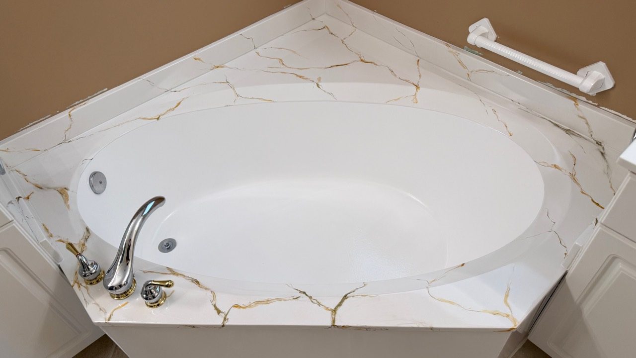 The finished corner tub — hand-veined marble-imitation deck around a bright white basin