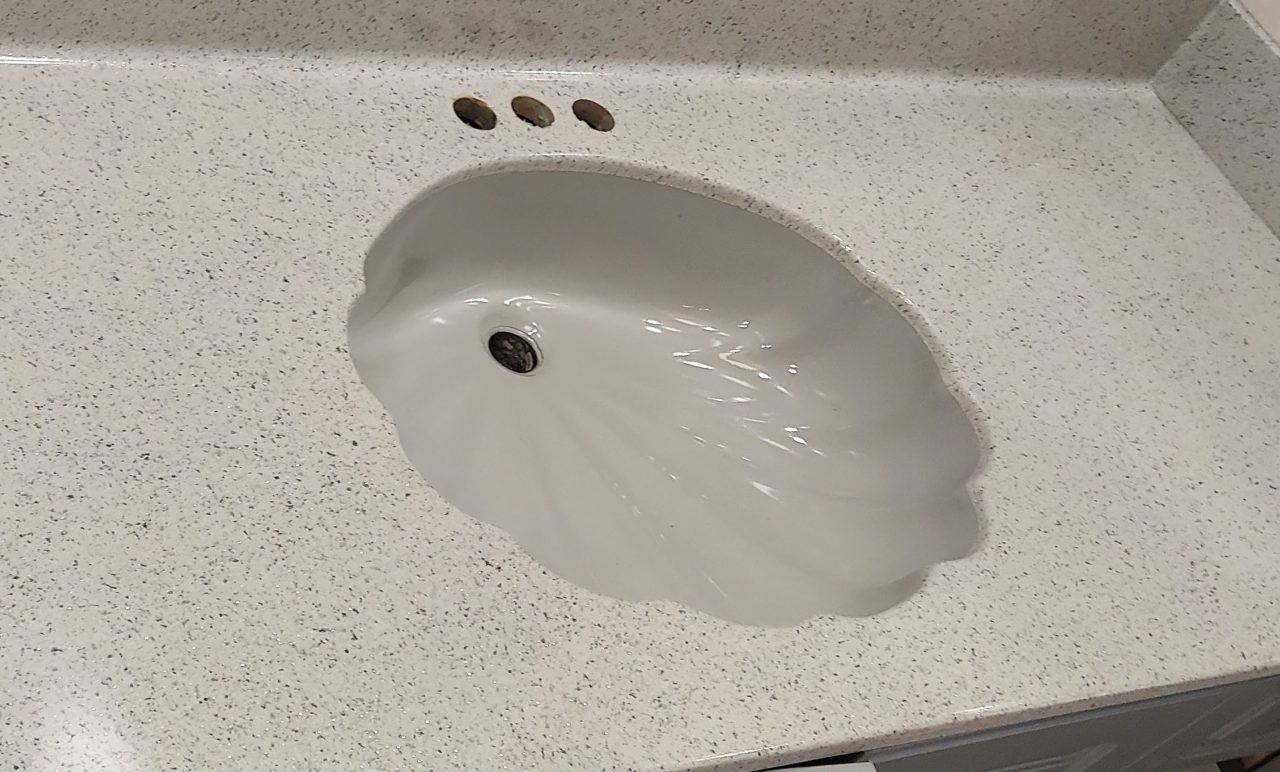 Clean shell-shaped bathroom sink and vanity top refinished in white speckle